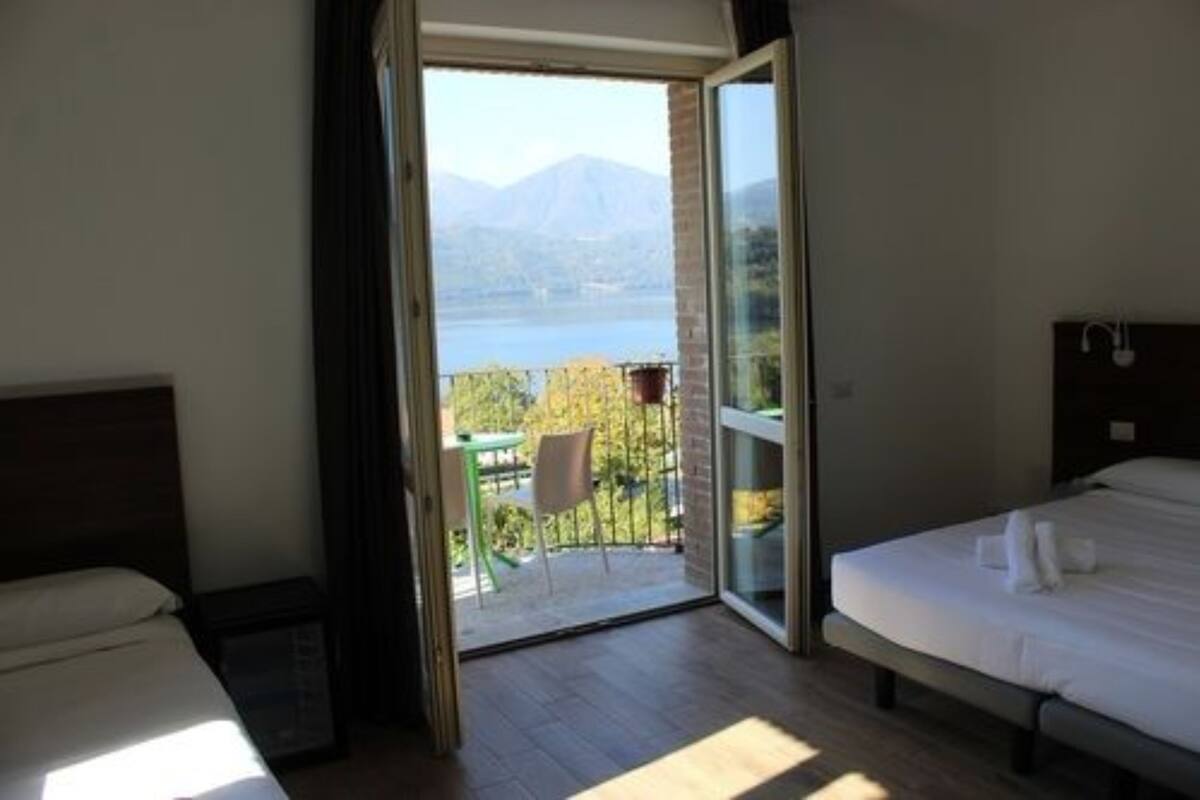 Une chambre à coucher avec un lit, une table de chevet et une vue sur une montagne et un lac, visible à travers une porte vitrée.