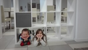 Un intérieur moderne avec des murs blancs et une étagère modulable blanche. On aperçoit des chaises et une table au fond.