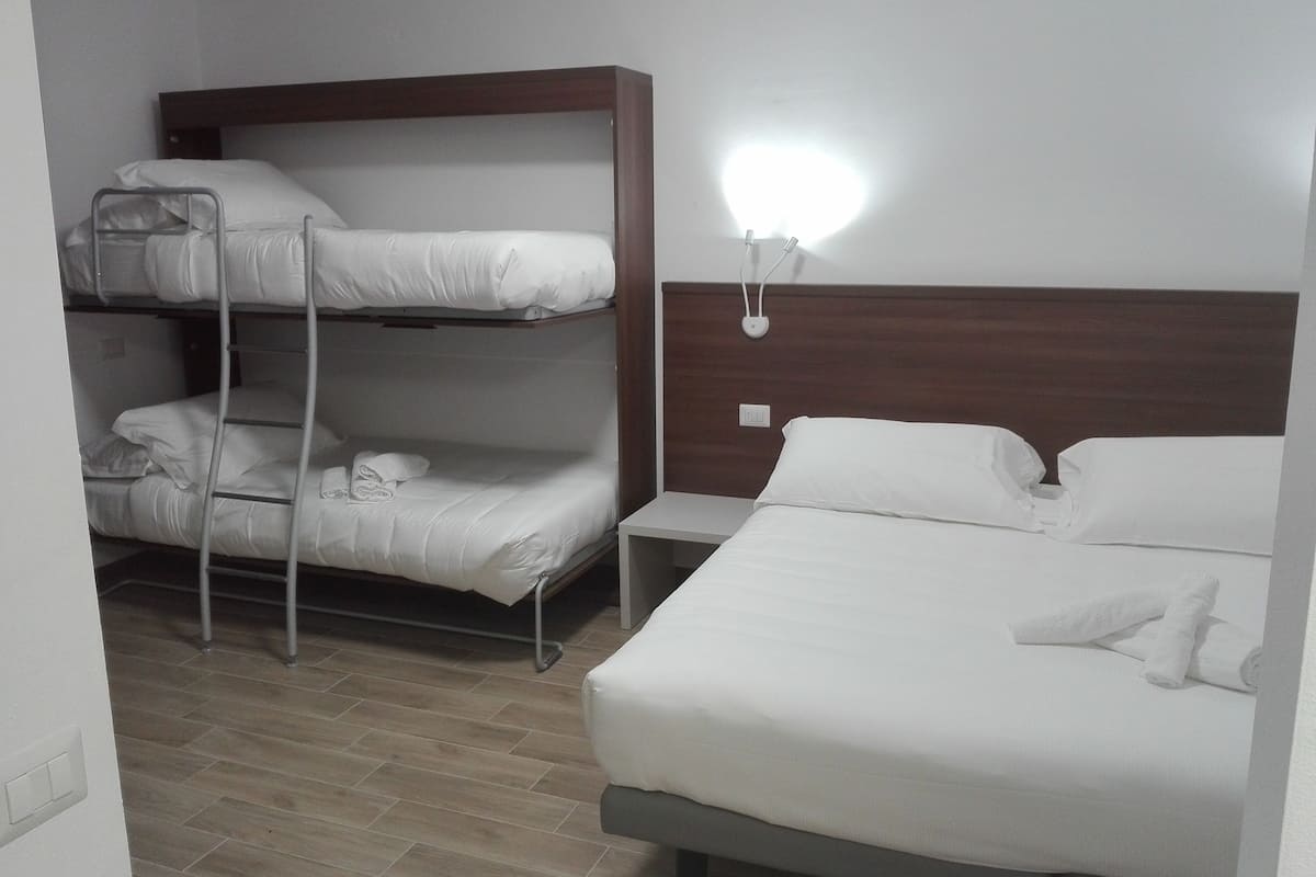 Une chambre d’hôtel équipée d’un lit superposé, d’un lit simple, d’une table de chevet et d’une lampe fixée au mur.