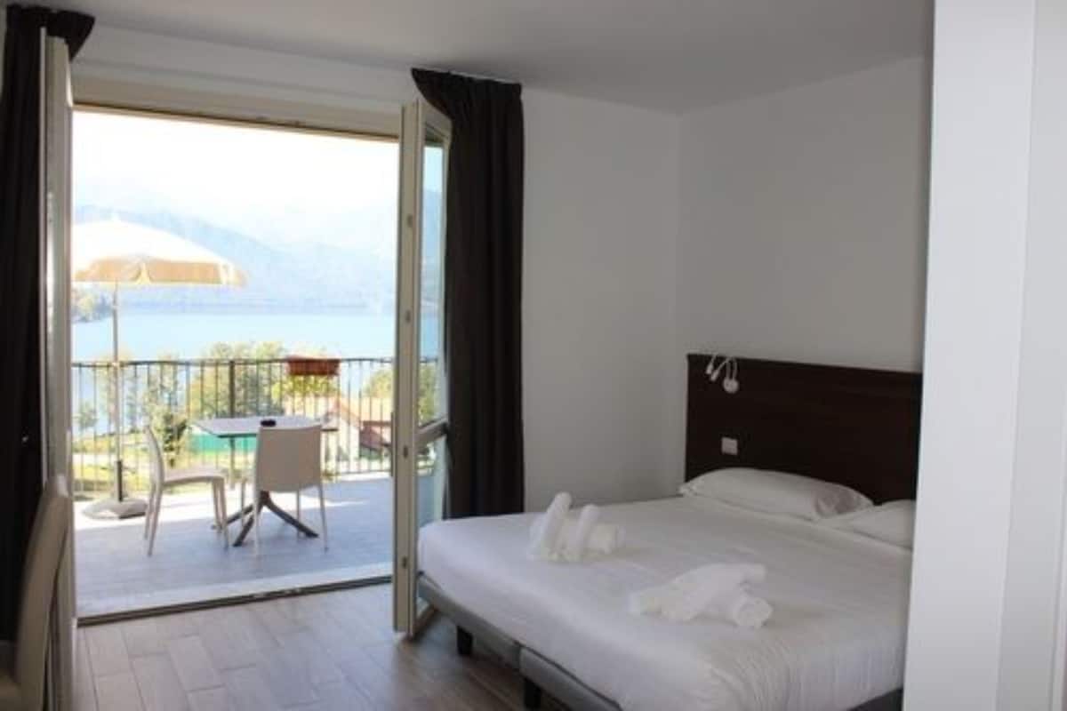 Une chambre d’hôtel avec un lit, une table et des chaises sur un balcon donnant sur la mer.