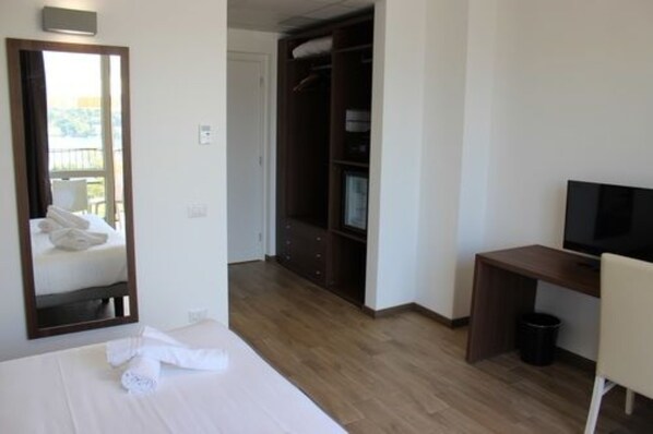 Una habitación de hotel con una cama, un escritorio con televisor, un armario y un espejo.