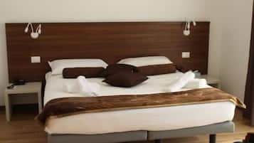 Una cama bien hecha con cabecera marrón, ropa de cama blanca y una manta marrón. Hay dos mesitas de noche con lámparas y un pequeño tocador con un teléfono.
