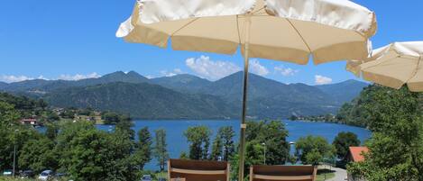Terraza con dos sillas bajo un paraguas grande, con vista a un lago y montañas.