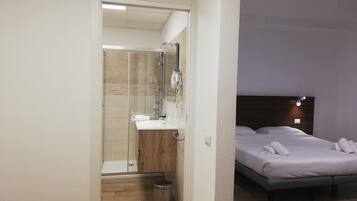 A hotel room with a shower, a wooden vanity, a bed with white linens, and a nightstand.