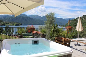 Un jacuzzi en un balcón con vistas a un lago y montañas al fondo.