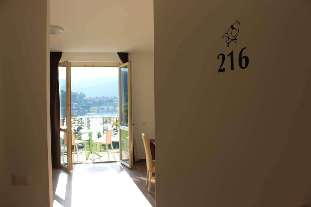 Une vue intérieure d’une chambre d’hôtel avec un balcon, une porte portant le numéro 216 et une vue sur l’extérieur.
