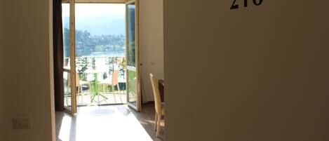 Une vue intérieure d’une chambre d’hôtel avec un balcon, une porte portant le numéro 216 et une vue sur l’extérieur.