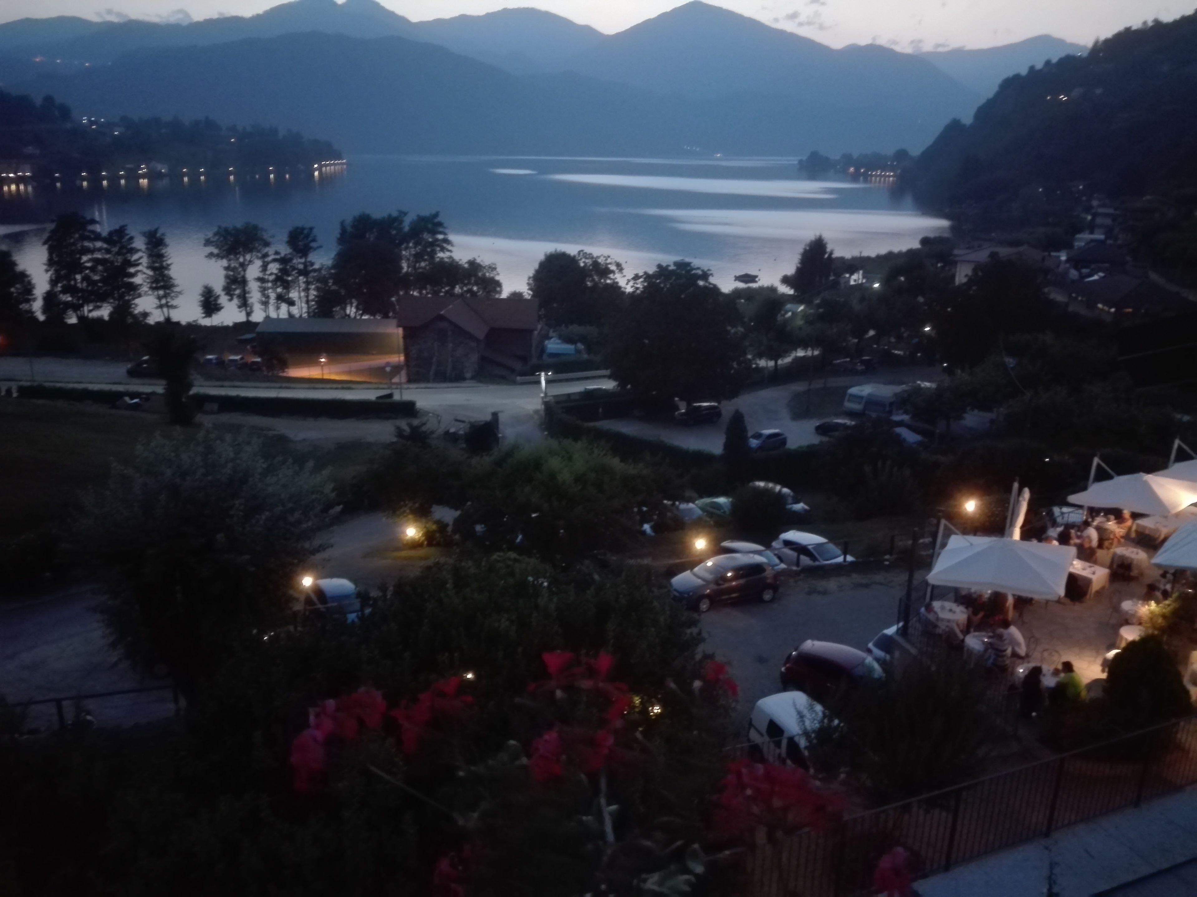 A lakeside view with a parking area, a building with a red roof, and a mountain range in the background.