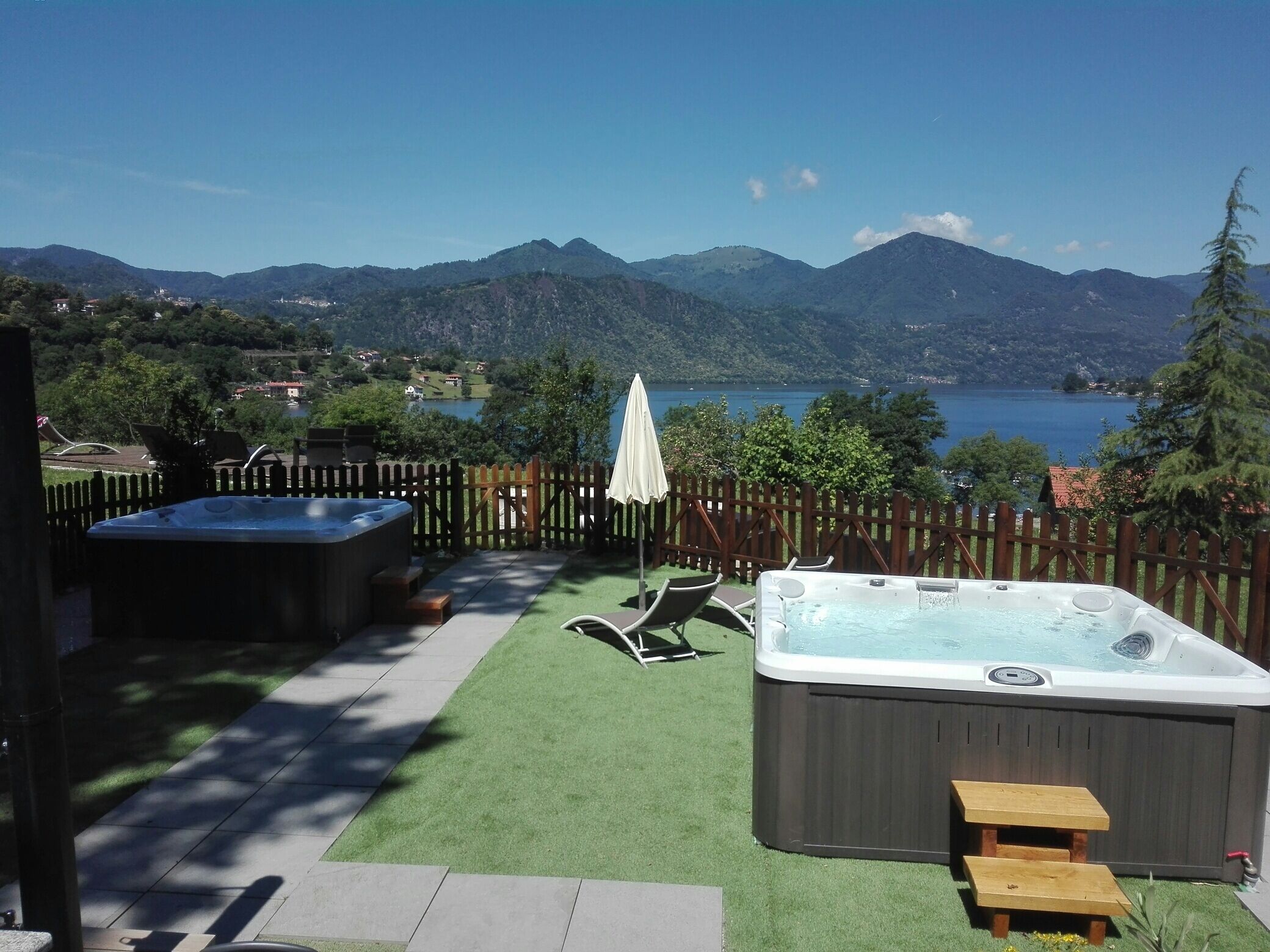Een achtertuin met twee whirlpools, een houten terras en uitzicht op bergen en een meer.