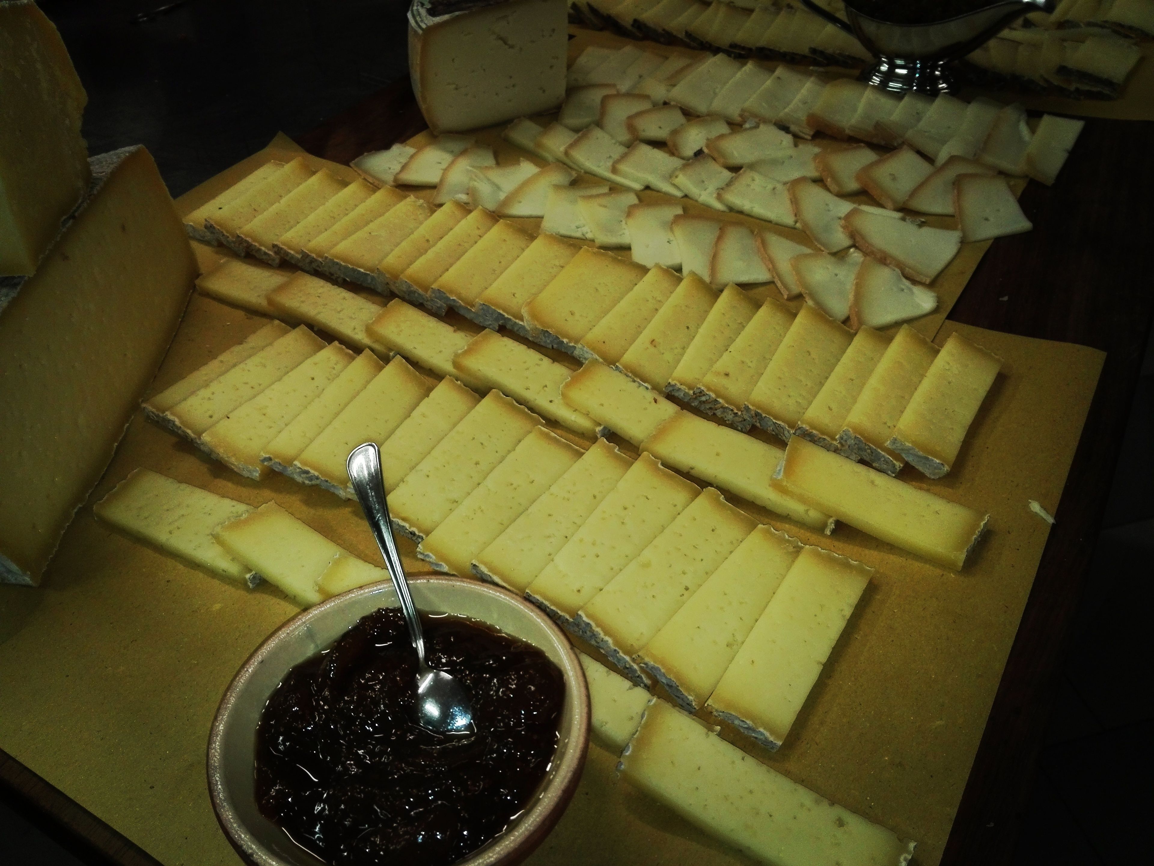 A cheese board with various types of cheese and a bowl of jam.