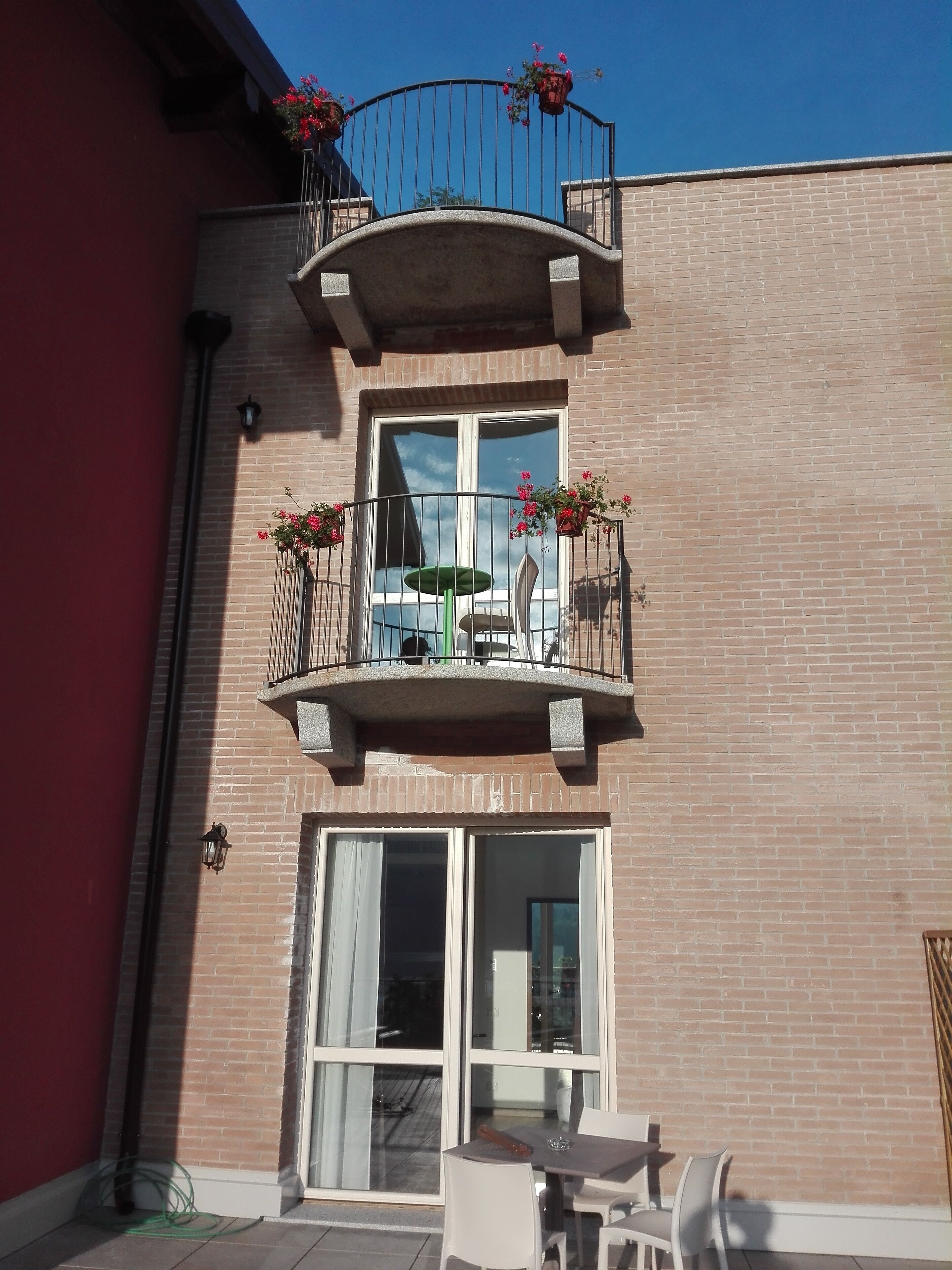 Un edificio de dos pisos con un balcón en el nivel superior, con plantas en macetas y una mesa con sillas.