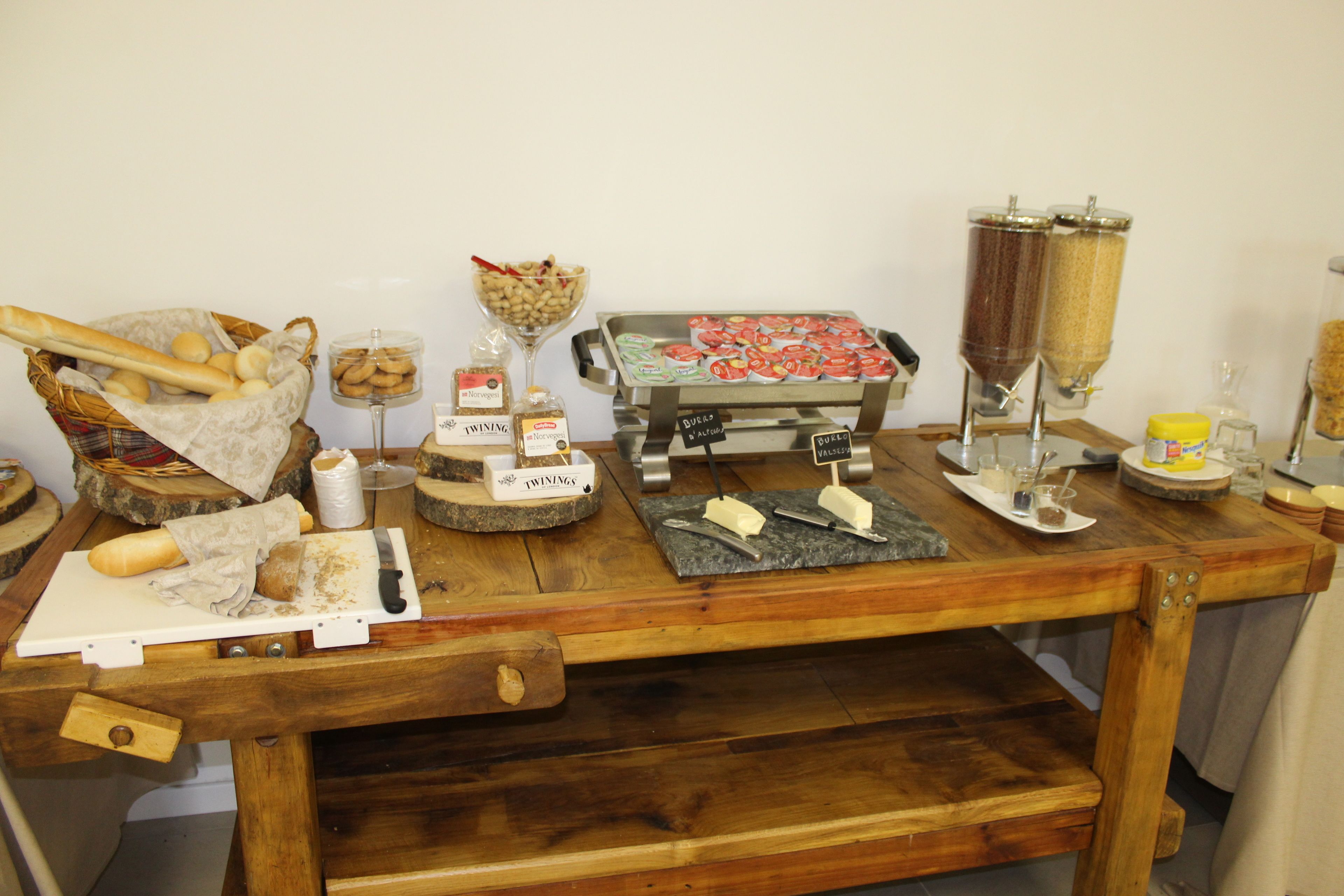 Une table en bois sur laquelle sont disposés divers aliments et condiments, notamment du pain, du fromage et des pots d’épices.