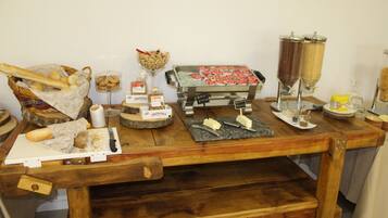 Une table en bois sur laquelle sont disposés divers aliments et condiments, notamment du pain, du fromage et des pots d’épices.