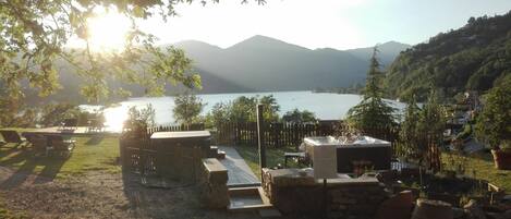 Une terrasse au bord du lac avec des sièges d’extérieur, un jacuzzi et une cheminée en pierre.