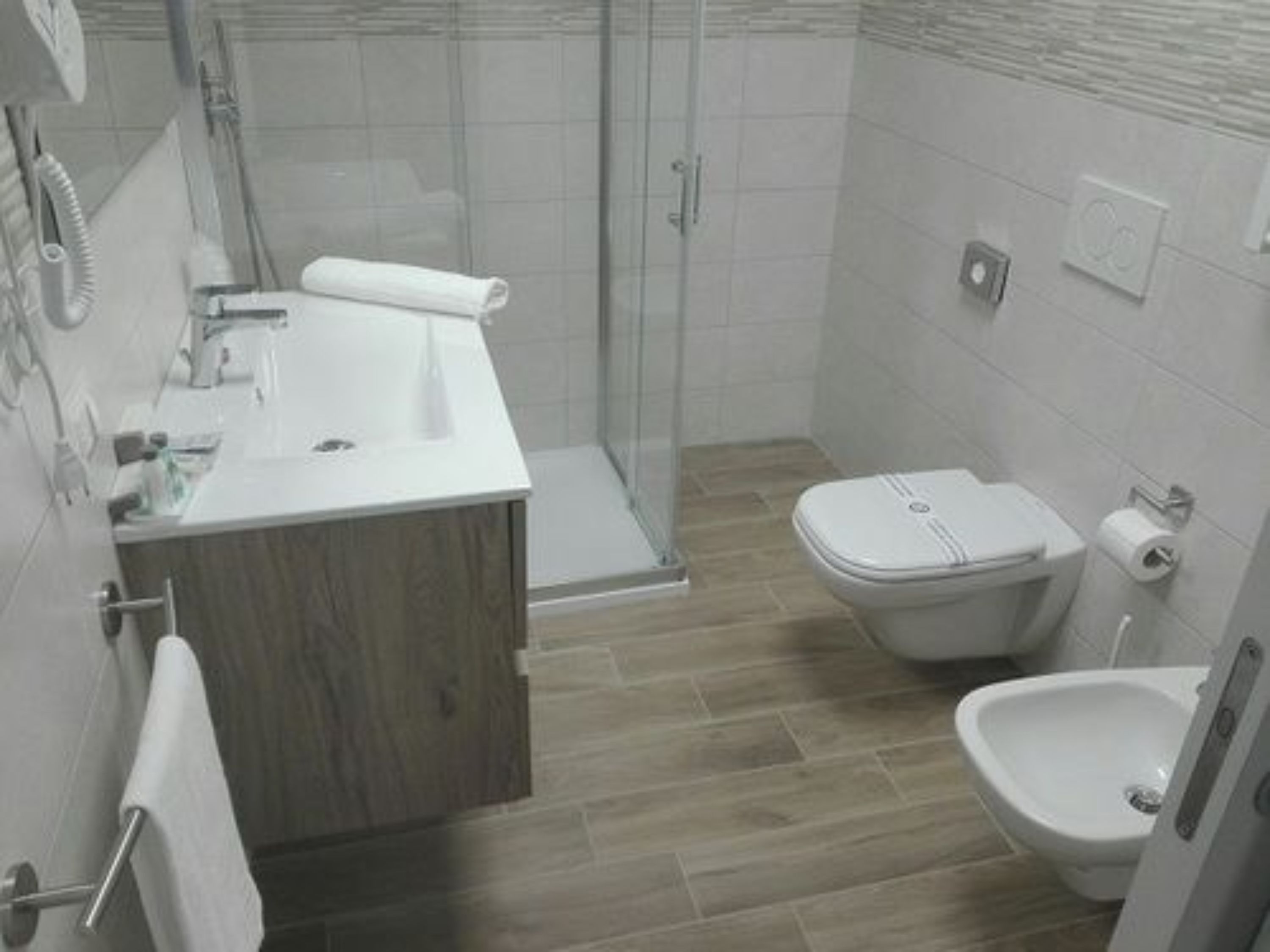 Une salle de bain moderne équipée d’une douche, de toilettes, d’un bidet et d’un meuble-lavabo en bois.