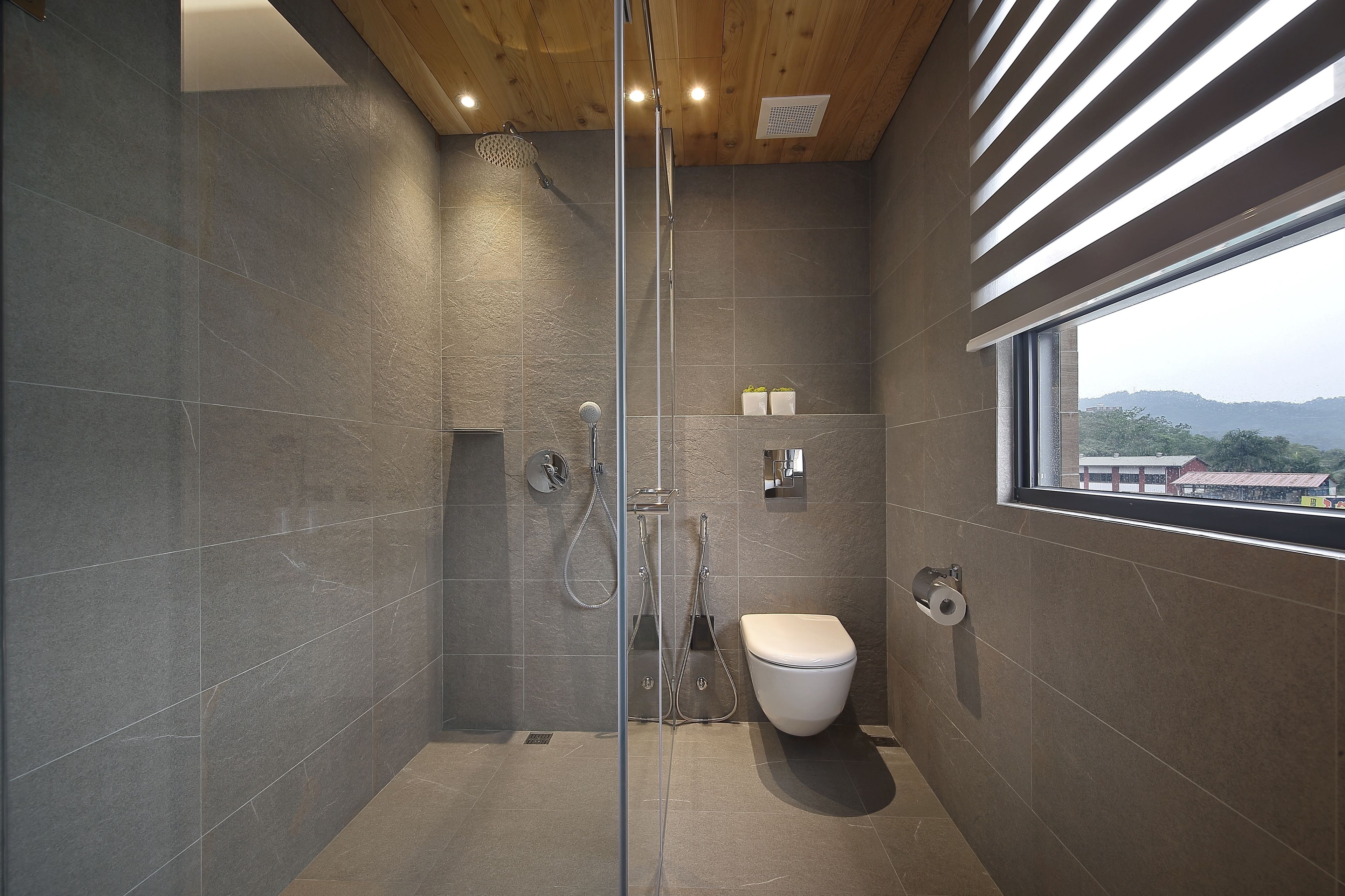 A modern bathroom with a glass shower enclosure, a toilet, and a window providing a view of the outside.