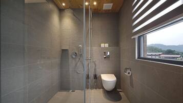 A modern bathroom with a glass shower enclosure, a toilet, and a window providing a view of the outside.
