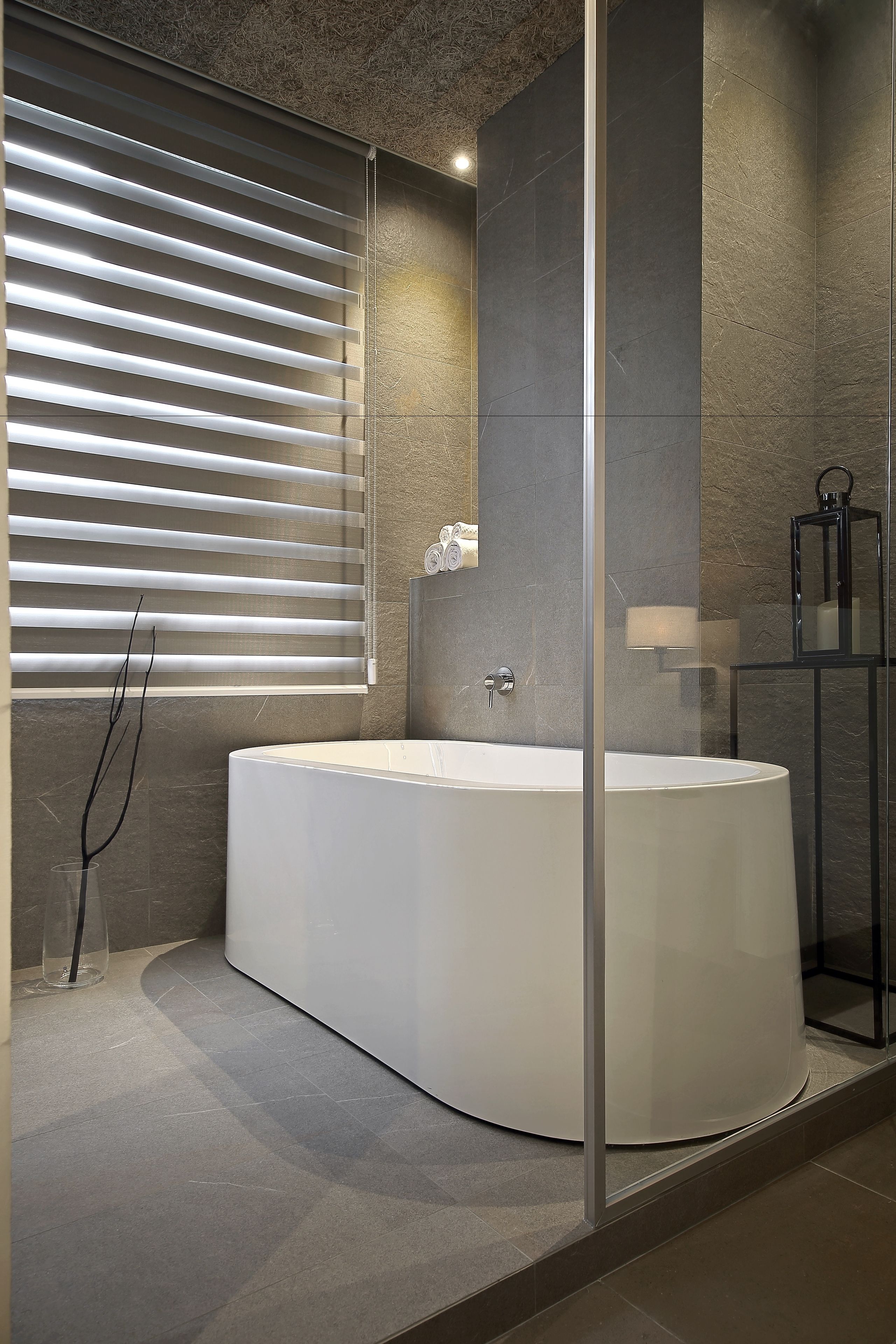 Une salle de bain moderne avec une grande baignoire, une douche en verre et une fenêtre avec des stores.