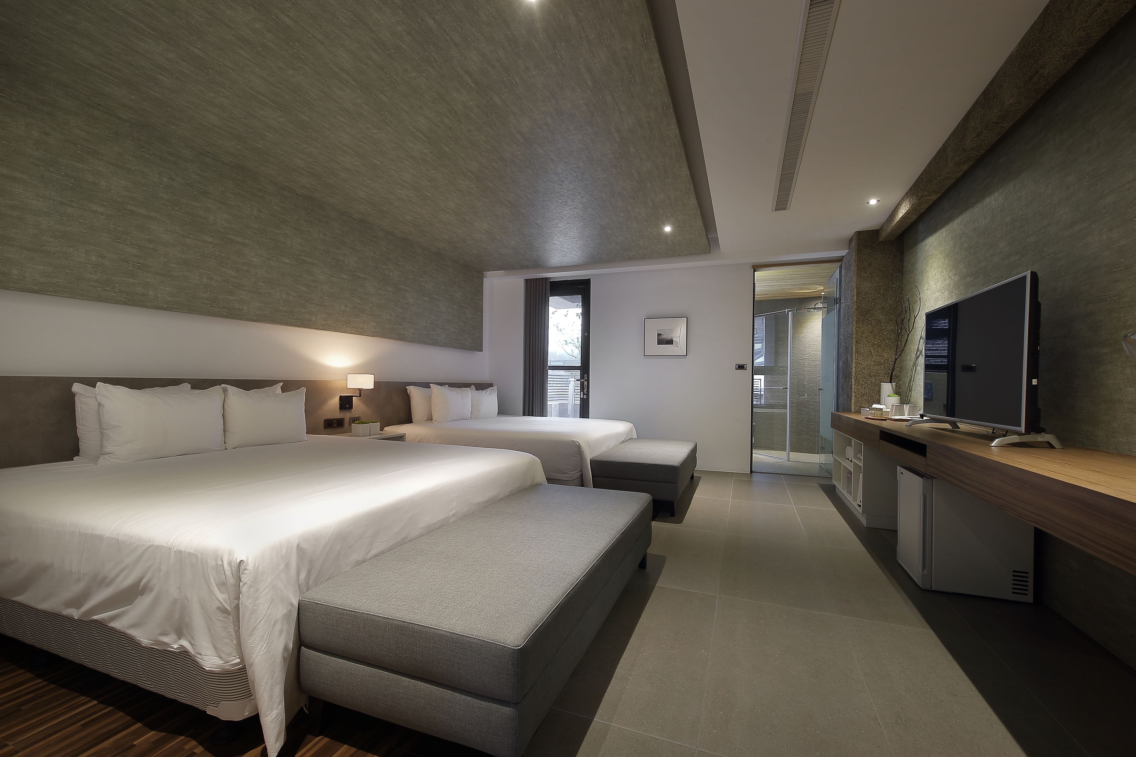 Una habitación de hotel moderna con una cama grande, una cama más pequeña, un sofá, un televisor y un escritorio.