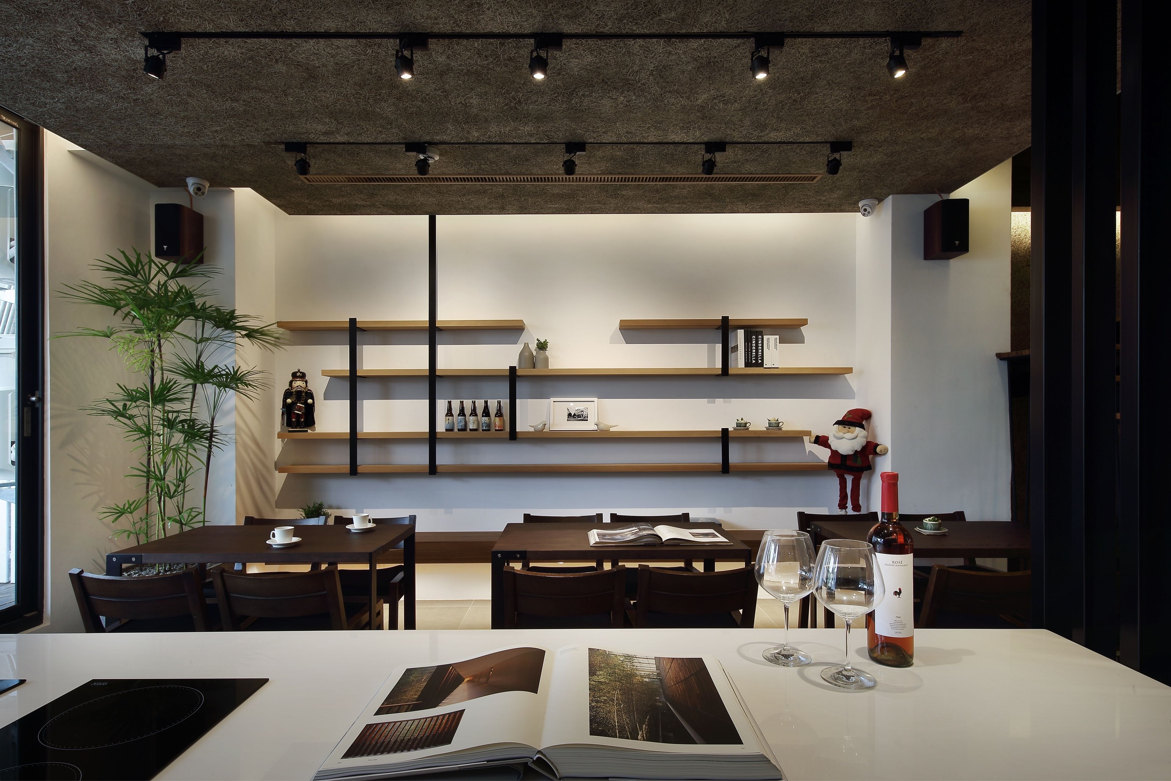 Un comedor moderno con mesas y sillas de madera, un ventanal grande y un estante en la pared con adornos.