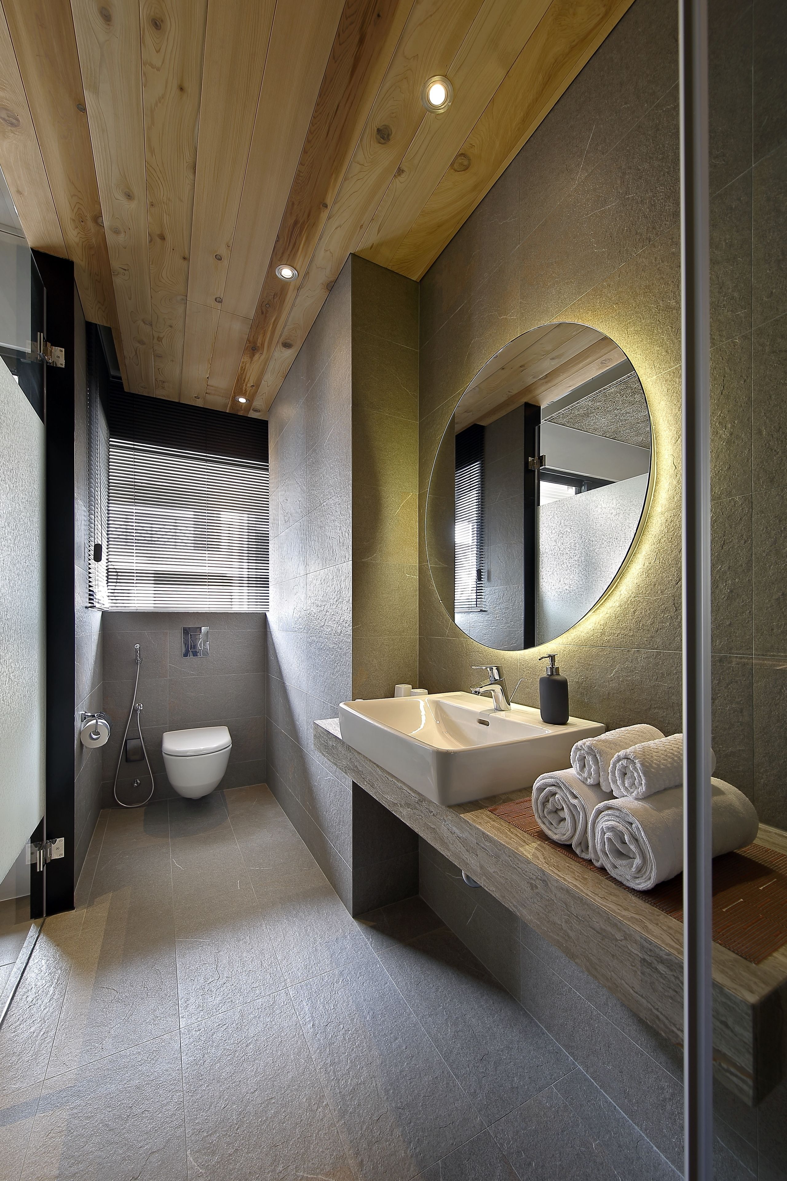 A modern bathroom with a wooden ceiling, a large mirror, a white sink, and a toilet.