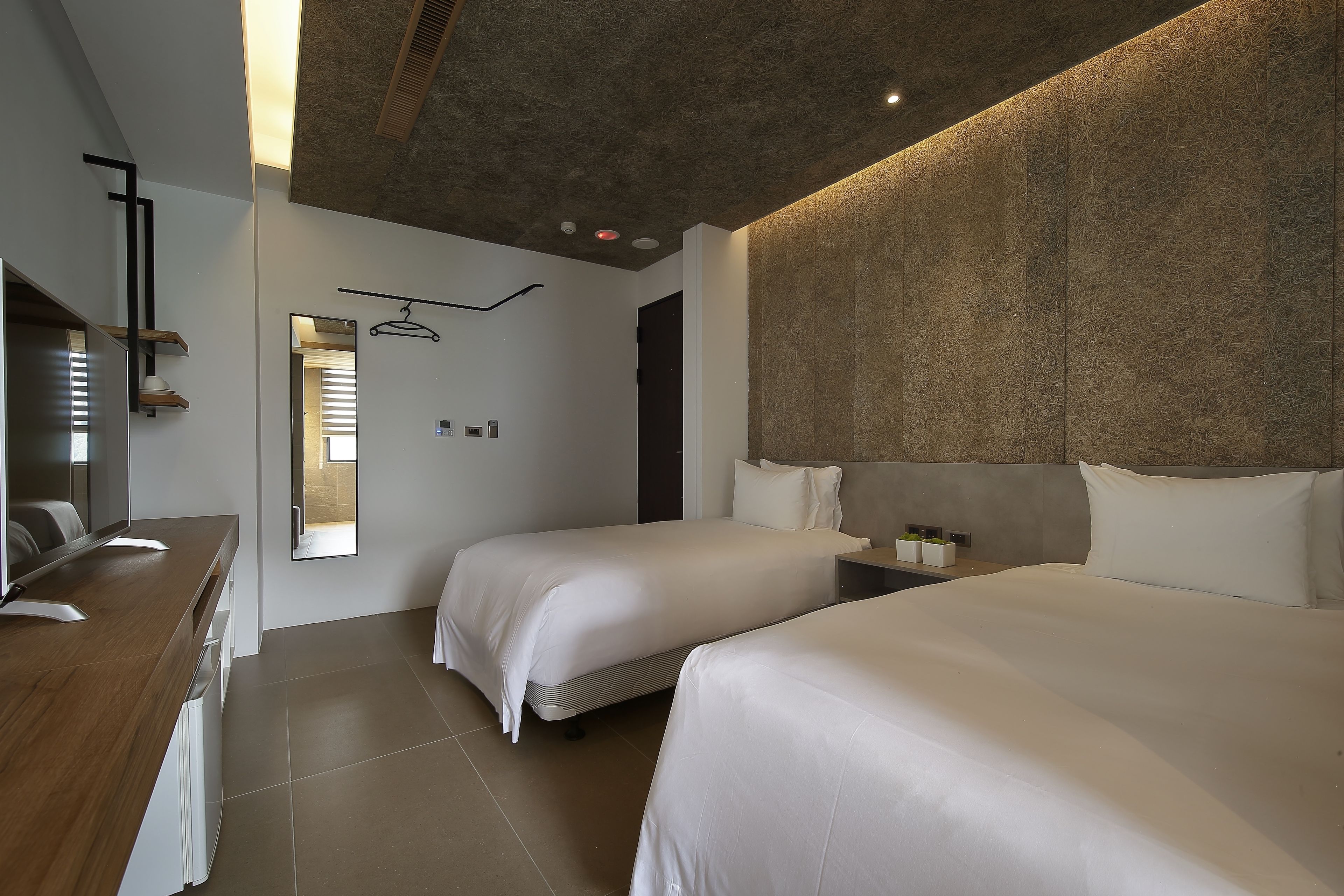 A modern hotel room with two beds, a wooden dresser, and a large mirror.