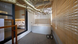 Een moderne badkamer met een ruime badkuip, een houten bankje en een decoratieve tak aan het plafond.