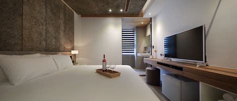 Habitación de hotel moderna con una cama grande, un televisor de pantalla plana, una mesita de madera y un banco empotrado.