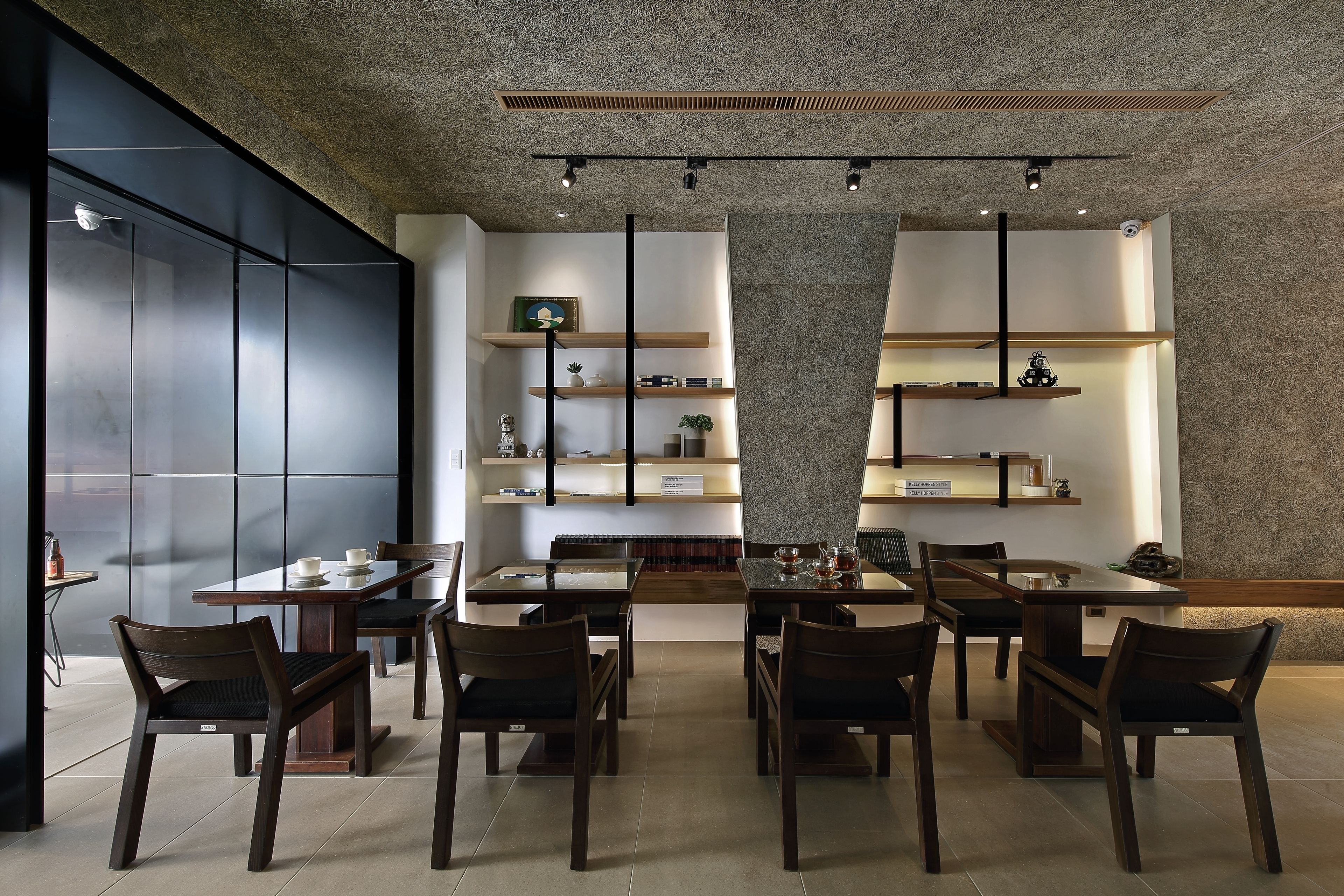 A modern dining area with multiple tables and chairs, built-in shelves with decorative items, and a textured ceiling.