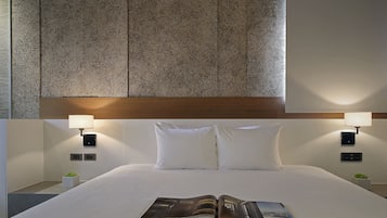 A neatly made bed with white linens and pillows, a magazine on the bed, and two bedside lamps.