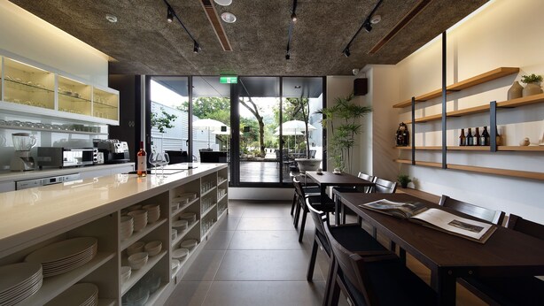 Een moderne keuken met een lange aanrecht, planken met servies en een eethoek met een tafel en stoelen.