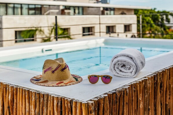 Uma área à beira da piscina com chapéu, óculos de sol e toalha sobre um deck de madeira.