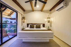 Quarto com cama grande, vigas de madeira no teto, aparelho de ar condicionado e vista de um edifício através de uma porta de vidro.