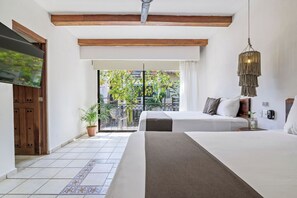 Habitación de hotel con dos camas, un televisor, un balcón con vistas a árboles y una lámpara colgante.