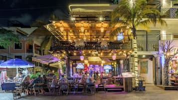 Un área de comedor al aire libre con mesas y sillas, una zona de estar techada y un bar.