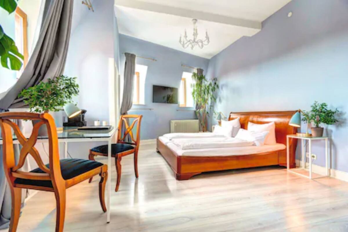 A bedroom with a wooden bed, a desk, chairs, and potted plants.
