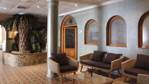 A lobby with wicker furniture, a palm tree, and a stone wall. - Aparthotel Sole Bello (Torrevieja)