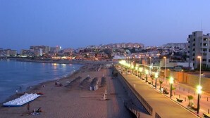 A beachside promenade with a row of street lamps, a sandy beach, and buildings in the background. - Aparthotel Sole Bello (Torrevieja)