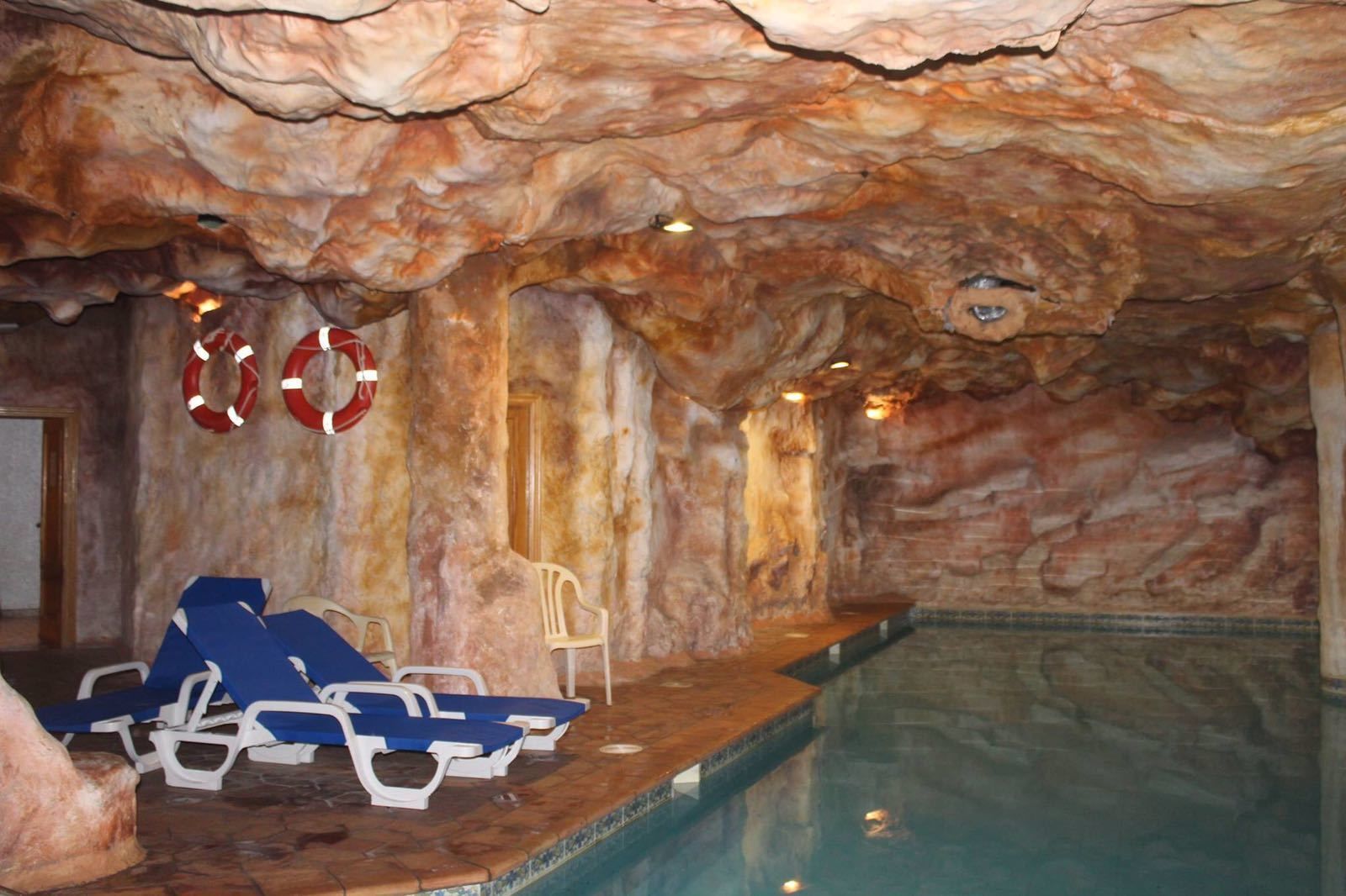 Une piscine intérieure avec des murs qui ressemblent à des rochers, des bouées de sauvetage et des chaises longues.