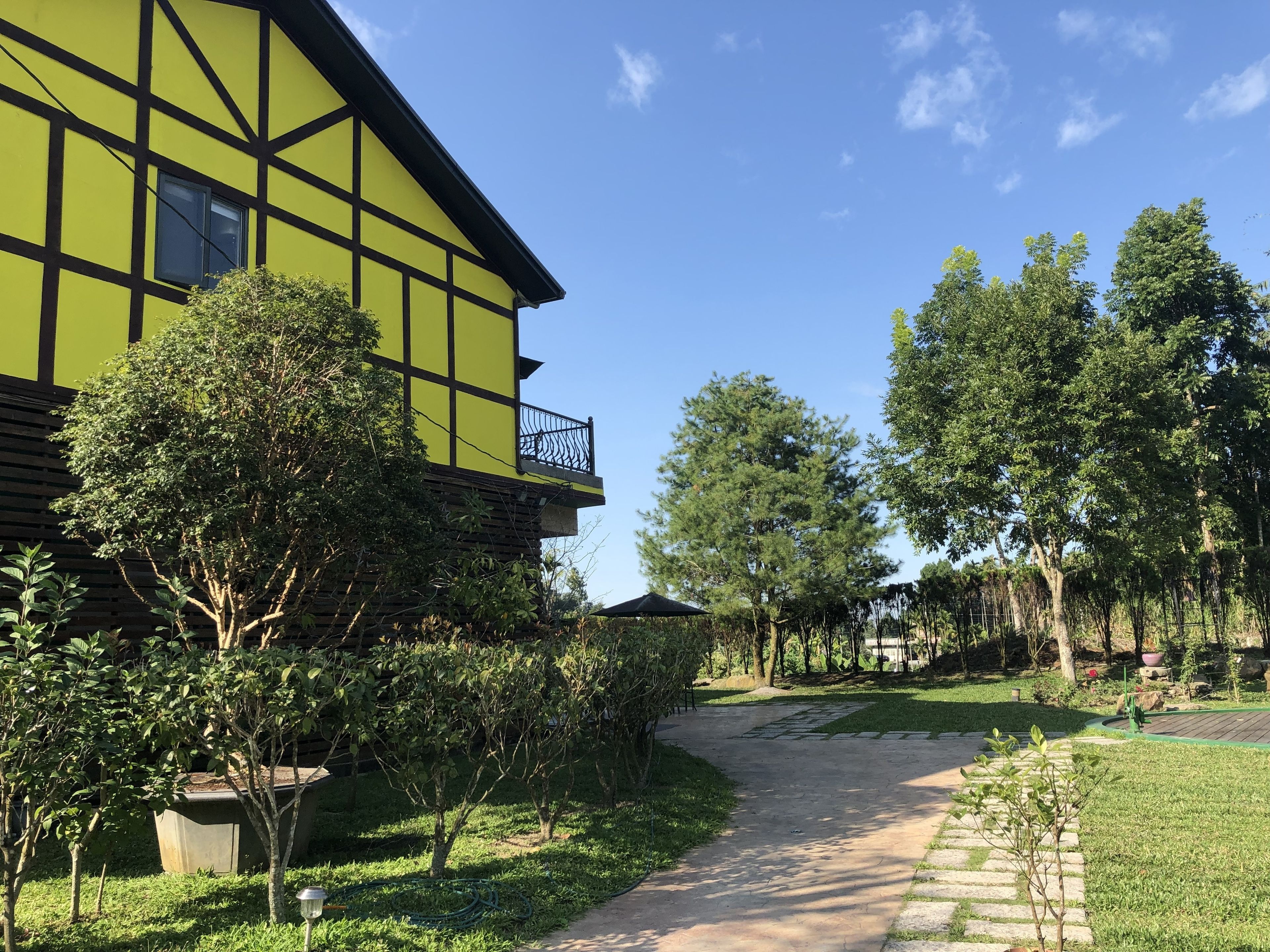 A green building with a balcony, surrounded by trees and a pathway.
