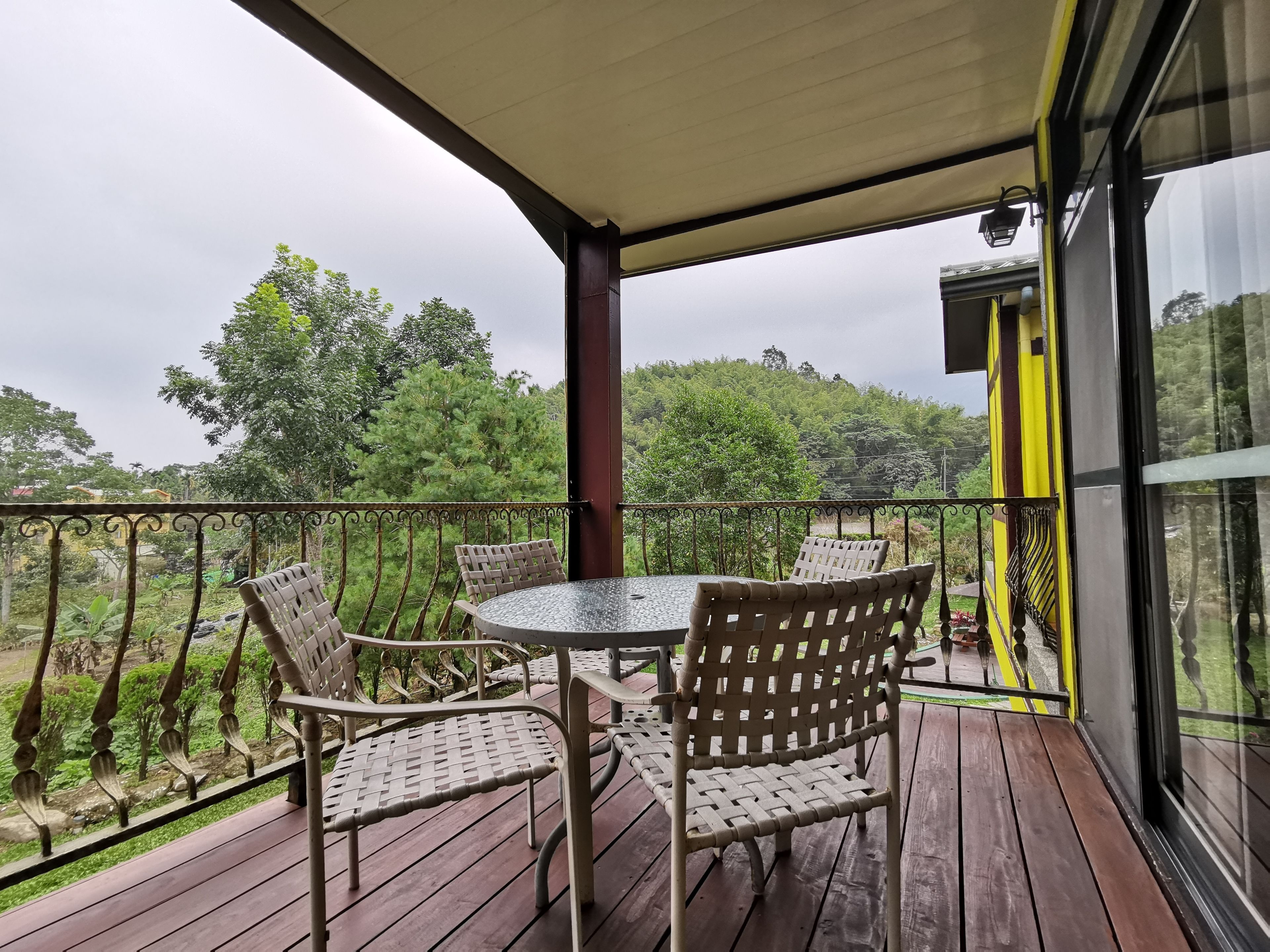 A covered outdoor area with a table and chairs, overlooking a lush green landscape.