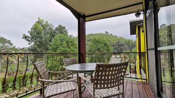 A covered outdoor area with a table and chairs, overlooking a lush green landscape.