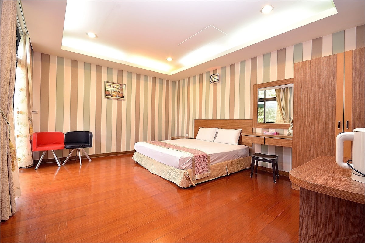 A hotel room with a bed, two chairs, a desk, and a mirror.
