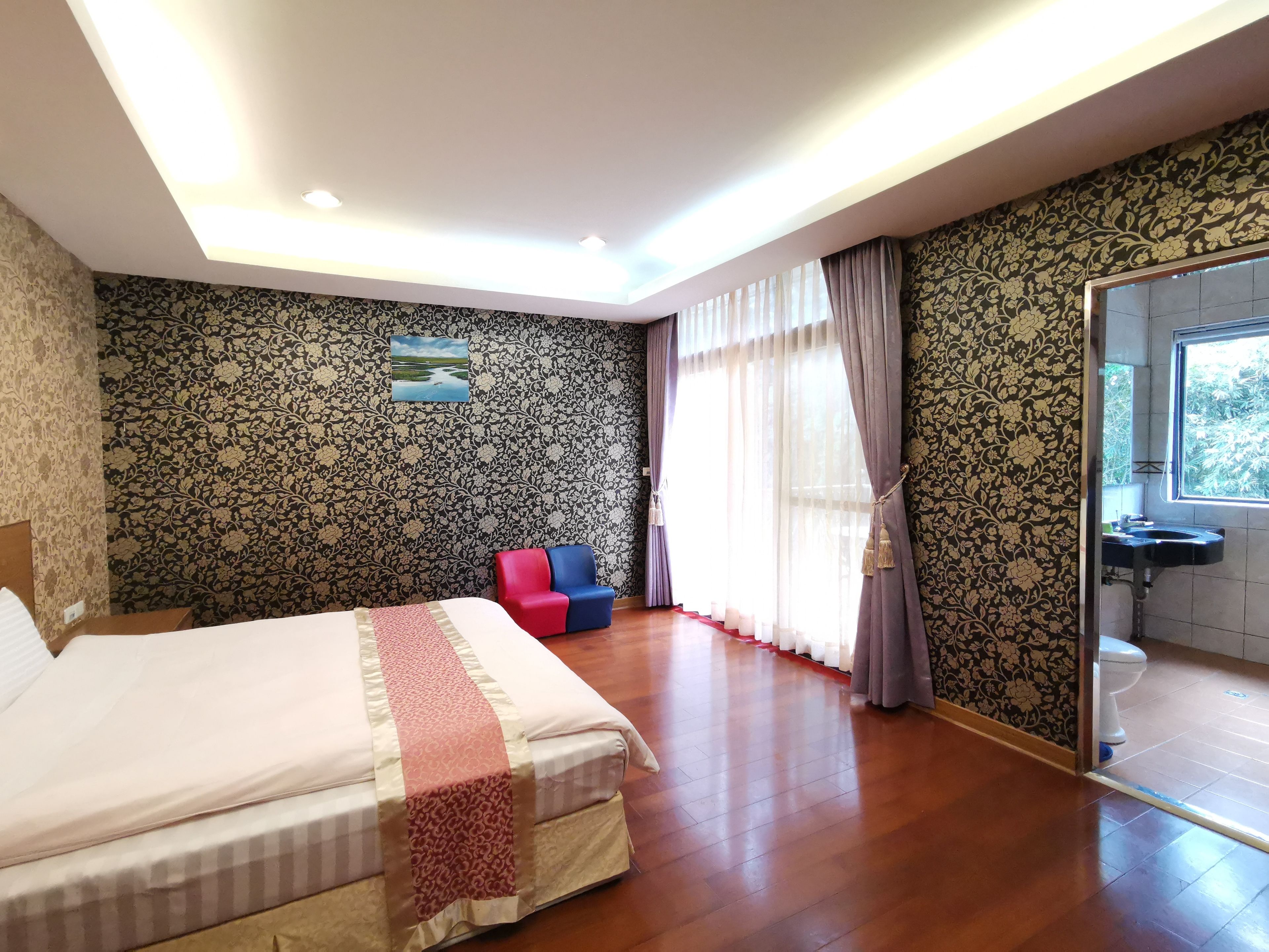 Habitación de hotel con una cama grande, un pequeño espacio para sentarse, un baño con lavabo y vistas al exterior.