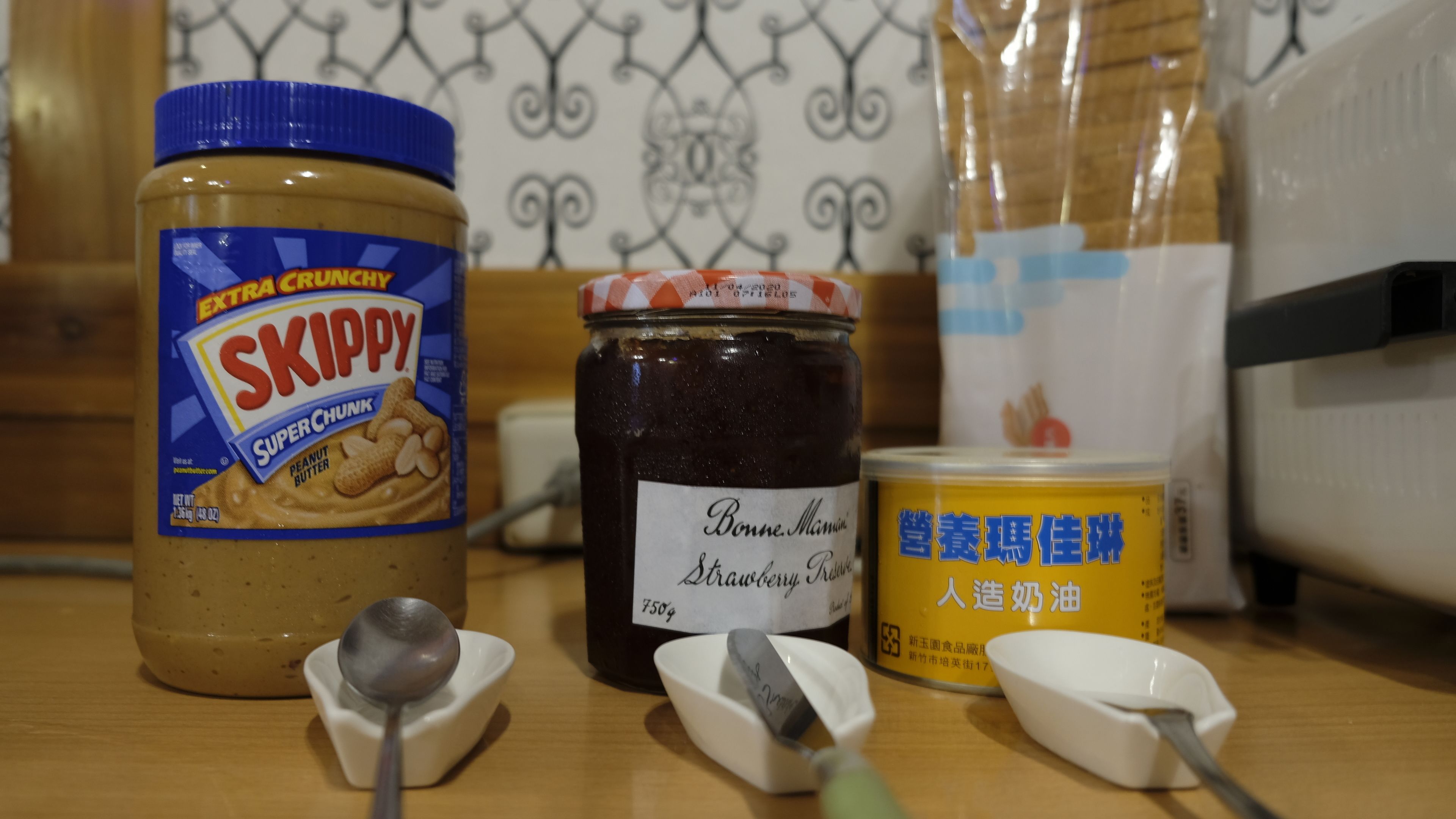 A kitchen counter with a jar of peanut butter, a jar of strawberry preserve, and a container of soy milk.