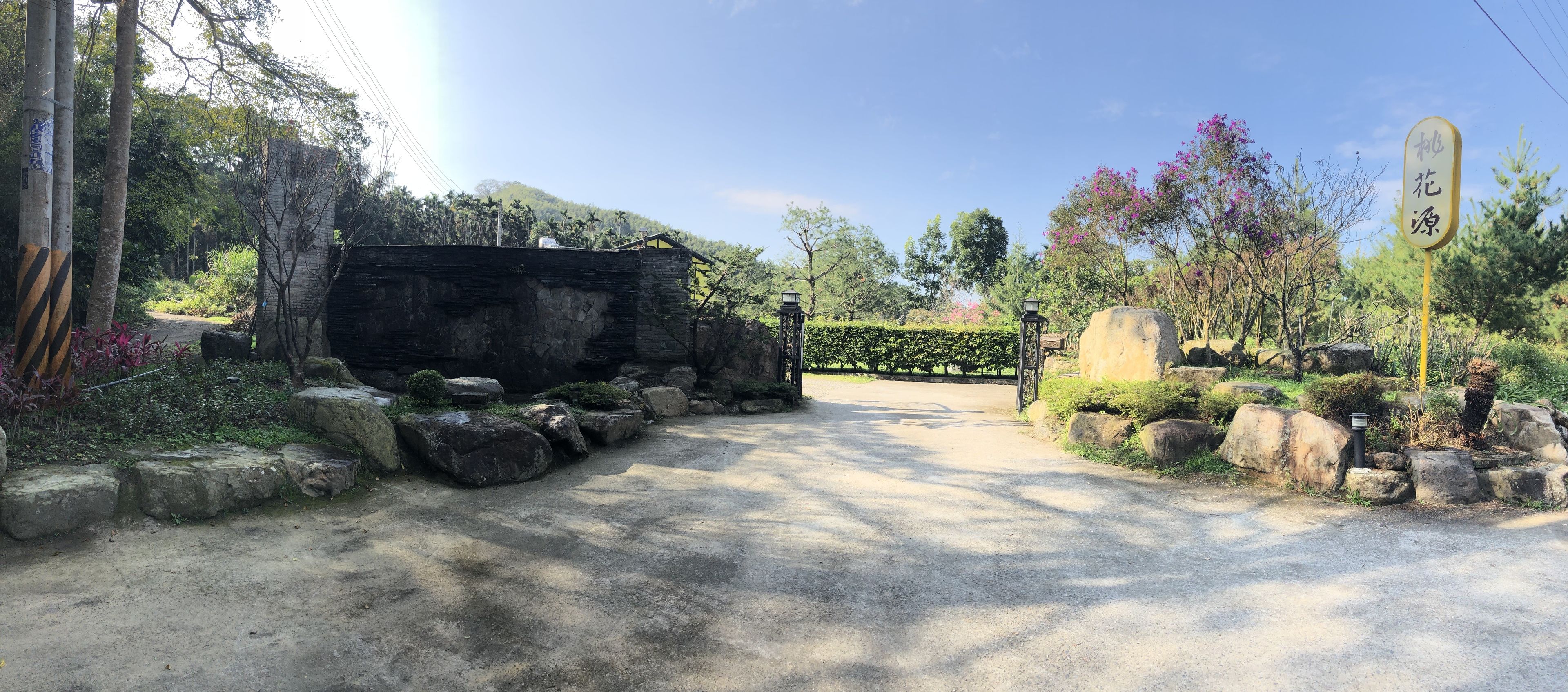 A paved pathway leading through a landscaped area with rocks and plants, a stone wall, and a signpost.