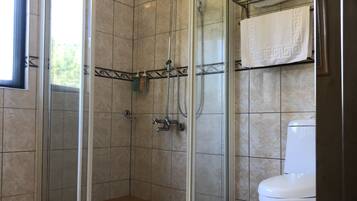 A bathroom with a glass-enclosed shower, a toilet, and a towel rack with folded towels.