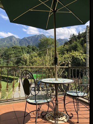 Une terrasse avec une table et des chaises, un parasol vert et une vue sur les montagnes.