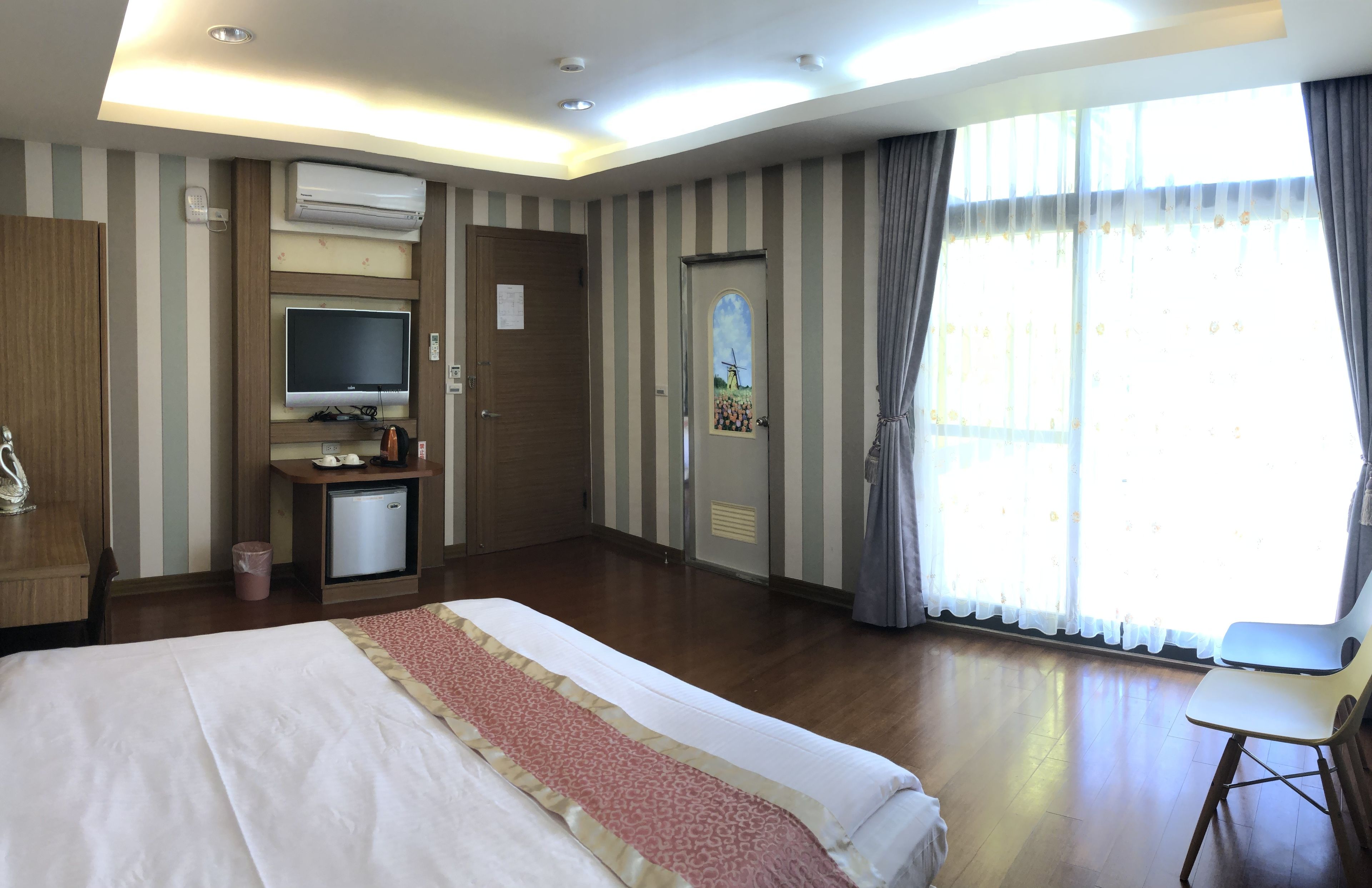 A hotel room with a bed, a desk with a computer, a TV, and a window with curtains.