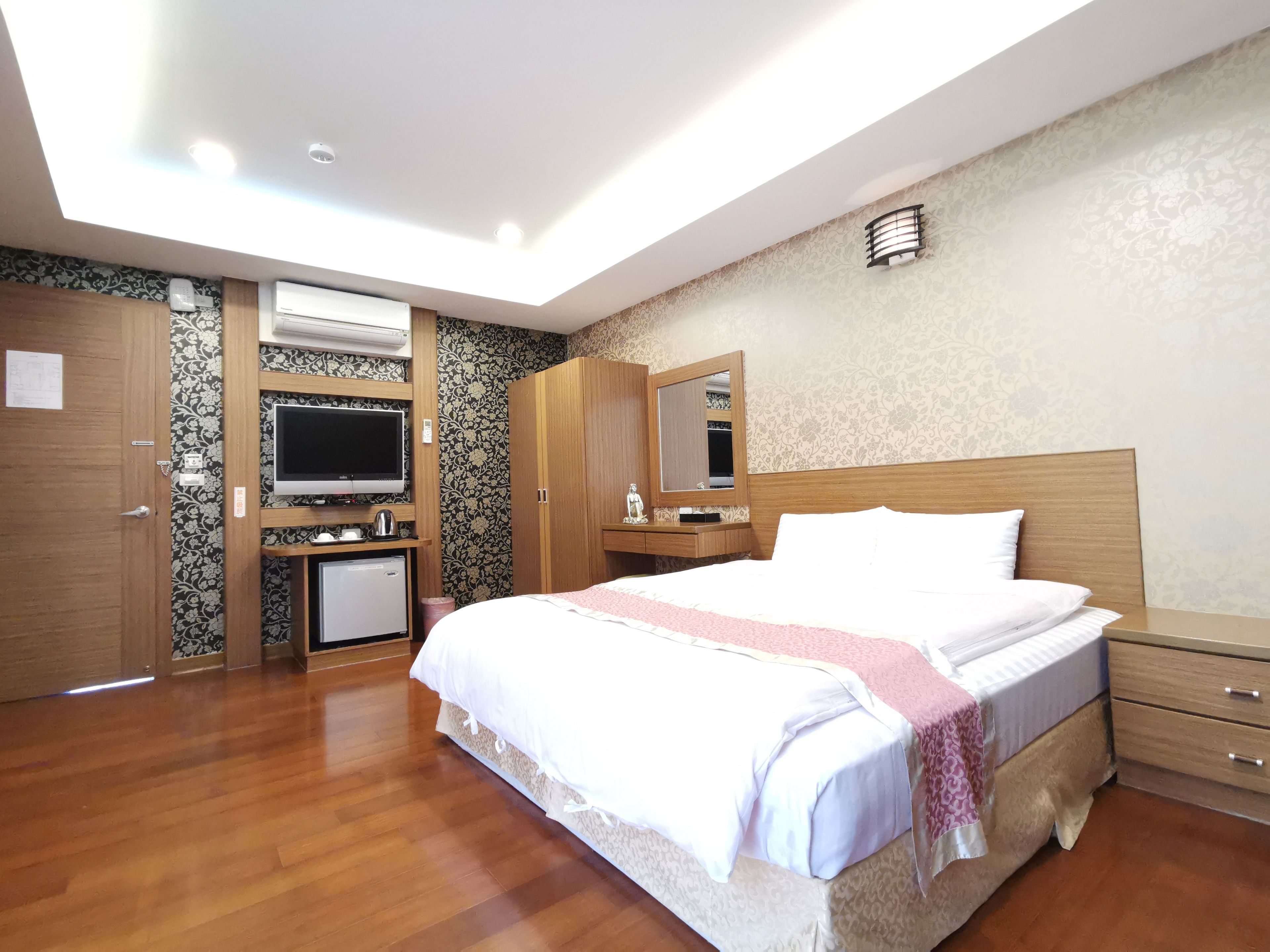 A hotel room with a bed, a TV, a desk with a computer, and a wardrobe.